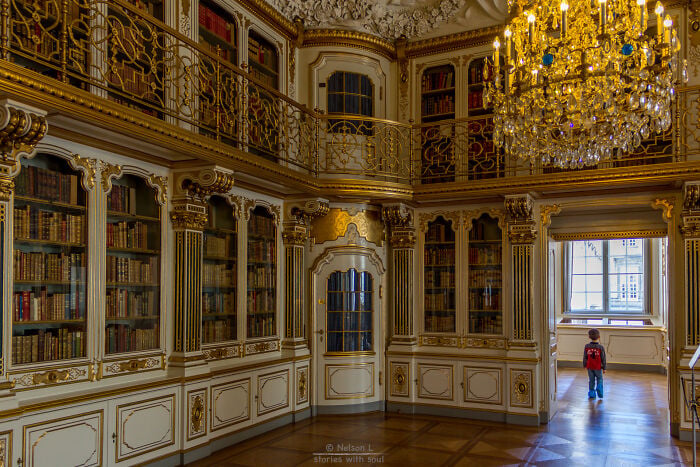 Grandiose Bibliothekseinrichtung mit aufwendigen Golddetails, hohen B&uuml;cherregalen und einem Kind, das eine magische Buchhandlung erkundet.