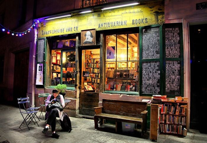 Gemütliche und prunkvolle Buchhandlung bei Nacht mit warmer Beleuchtung, gefüllt mit Büchern und einer lesenden Person draußen. Gemütliche und prunkvolle Buchhandlung bei Nacht mit warmer Beleuchtung, gefüllt mit Büchern und einer lesenden Person draußen.
