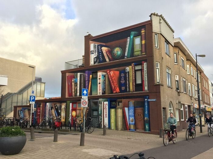 Geb&auml;udefassade bemalt mit riesigen, farbenfrohen B&uuml;chern, die eine magische Bibliotheks- und Buchhandlungsatmosph&auml;re in einer st&auml;dtischen Umgebung schaffen.