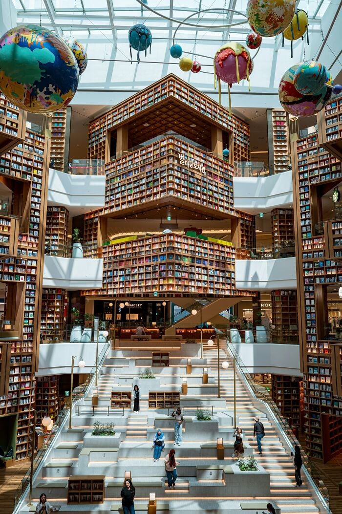 Grandiose Bibliothek im Inneren mit hohen Bücherregalen, großem Oberlicht und bunten Planetenskulpturen, die von der Decke hängen. Grandiose Bibliothek im Inneren mit hohen Bücherregalen, großem Oberlicht und bunten Planetenskulpturen, die von der Decke hängen.